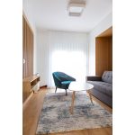 Светла дневна соба со сина фотеља и вградени дрвени ѕидни панели / Bright living room with blue armchair and built-in wooden wall panels.