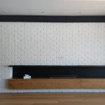 Минималистичка долга црна полица на бел ѕид со тули / Minimalist long black shelf on a white brick wall.