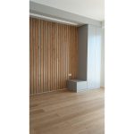 Ѕидна облога со дрвени летви до минималистички бел плакар / Wall cladding with wooden slats next to a minimalist white wardrobe.