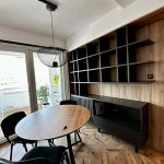 Трпезариски простор со црна маса и отворена дрвена полица за книги / Dining space with a black table and open wooden bookshelf.