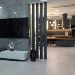 Поглед од кујна кон ТВ монтиран на преграда од дрвени летви / View from the kitchen toward a TV mounted on a wood slat divider.