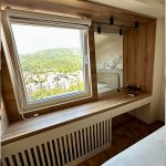 Работно биро поставено под прозорец со дрвени елементи / Work desk placed under a window with wooden elements